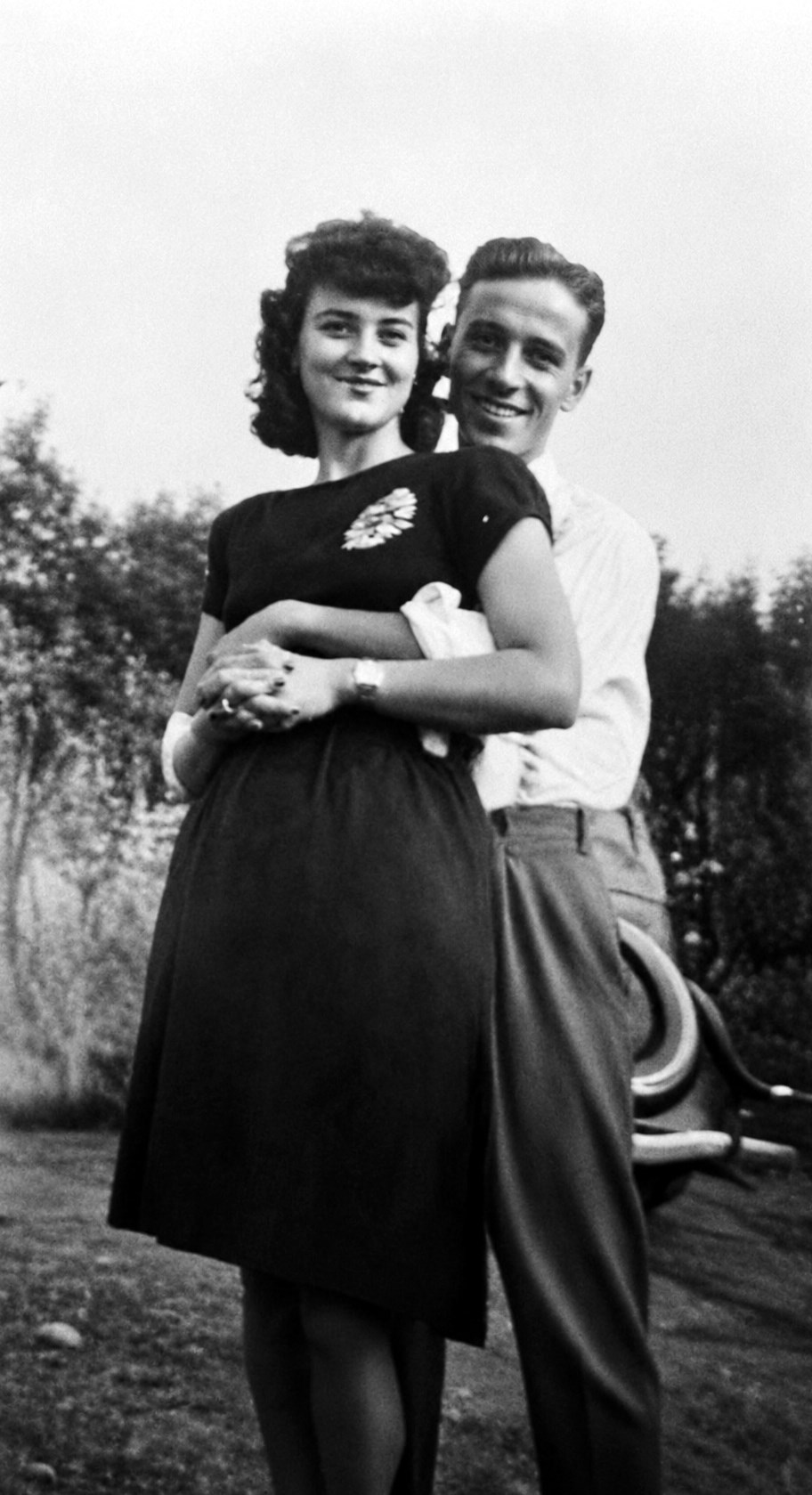 A young Helen and Leonard Fiedler outdoors in the 1940s, Leonard embracing Helen from behind as both smile at the camera.