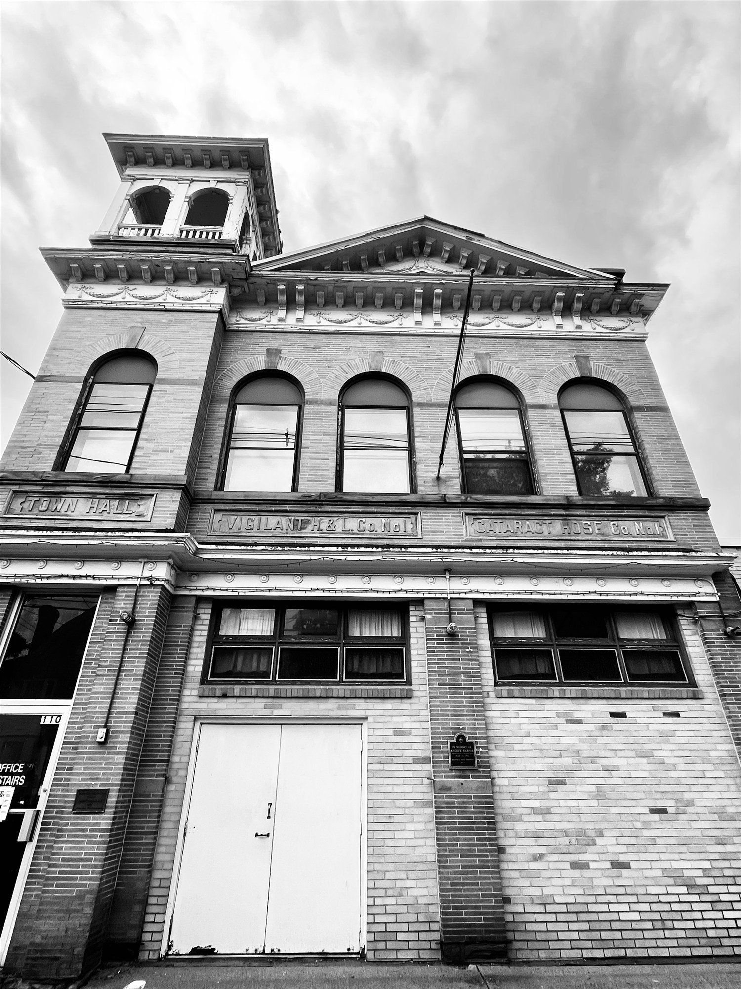 Looking up the brick facade of the old Town Hall firehouse, its stone lintels carved Town Hall, Vigilant H. & L. Co. No. 1, and Cataract Hose Co. No. 1, beneath the cupola.