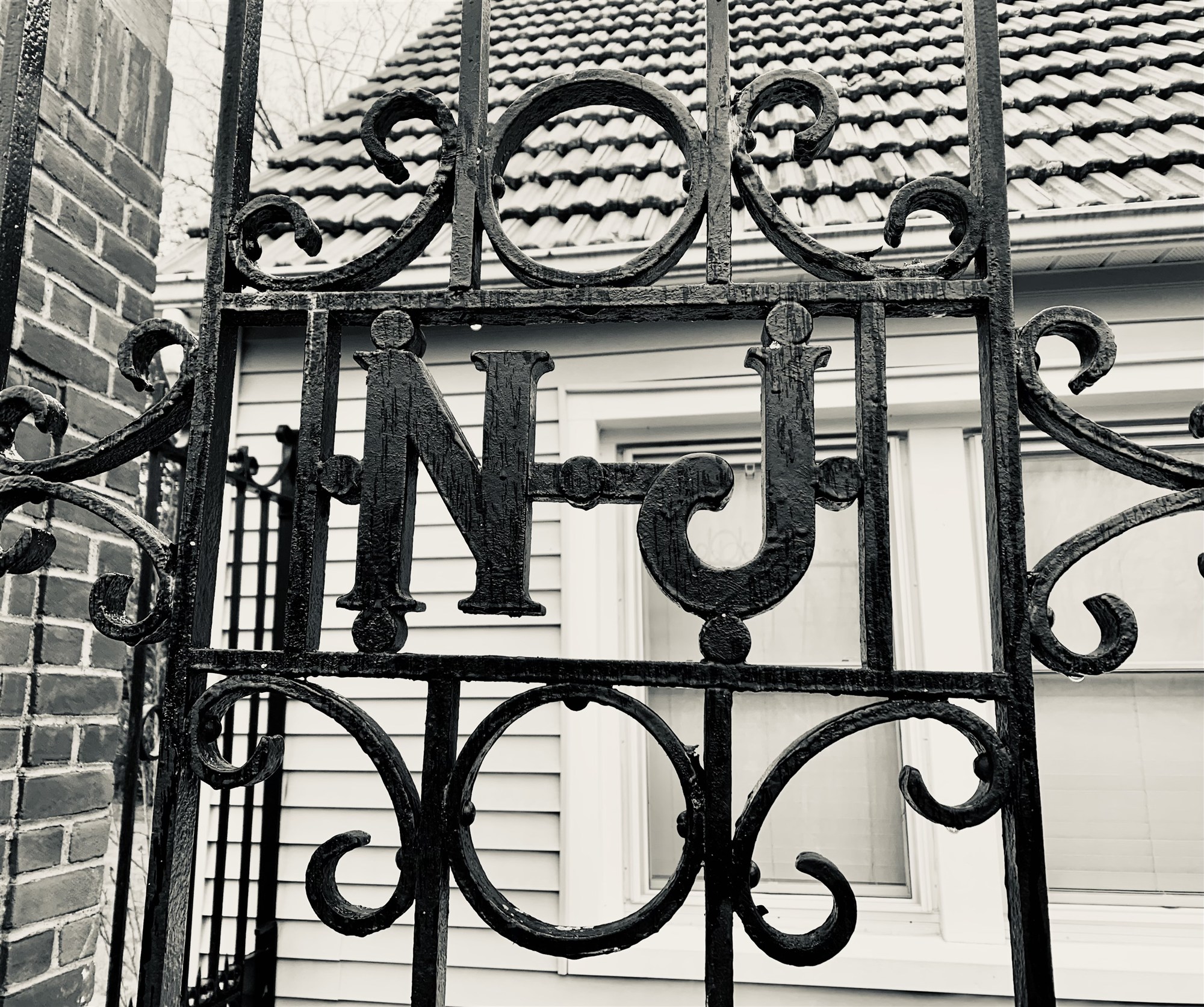 A close view of the hatchery's wrought-iron gate, the letters N and J worked into ornate scrolls, rain-wet and glistening.