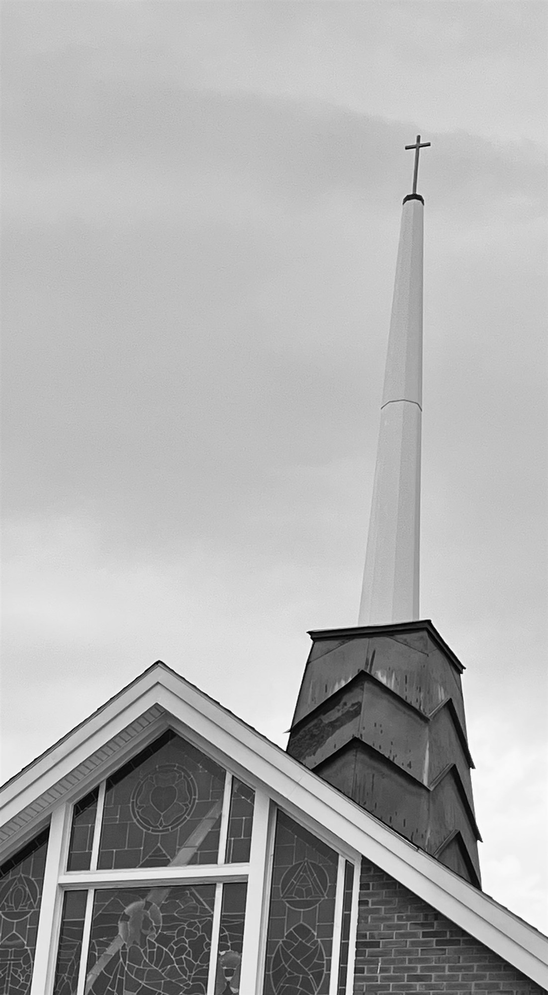 The slender white spire of Gethsemane Lutheran rising above a stained-glass gable window bearing the Luther rose.