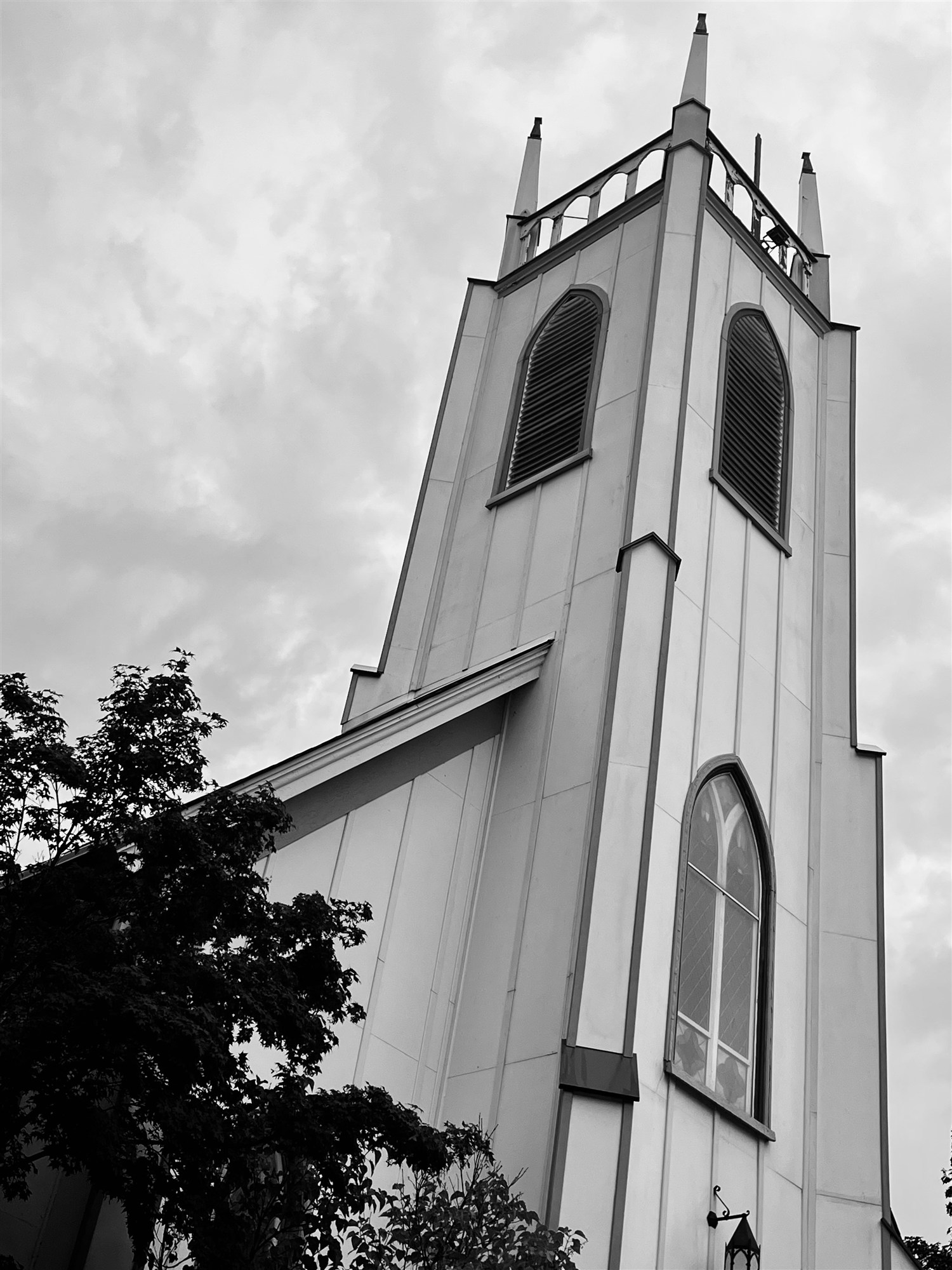 The white board-and-batten tower of St. James Episcopal Church, its Gothic pinnacles and arched louvers rising above the trees.