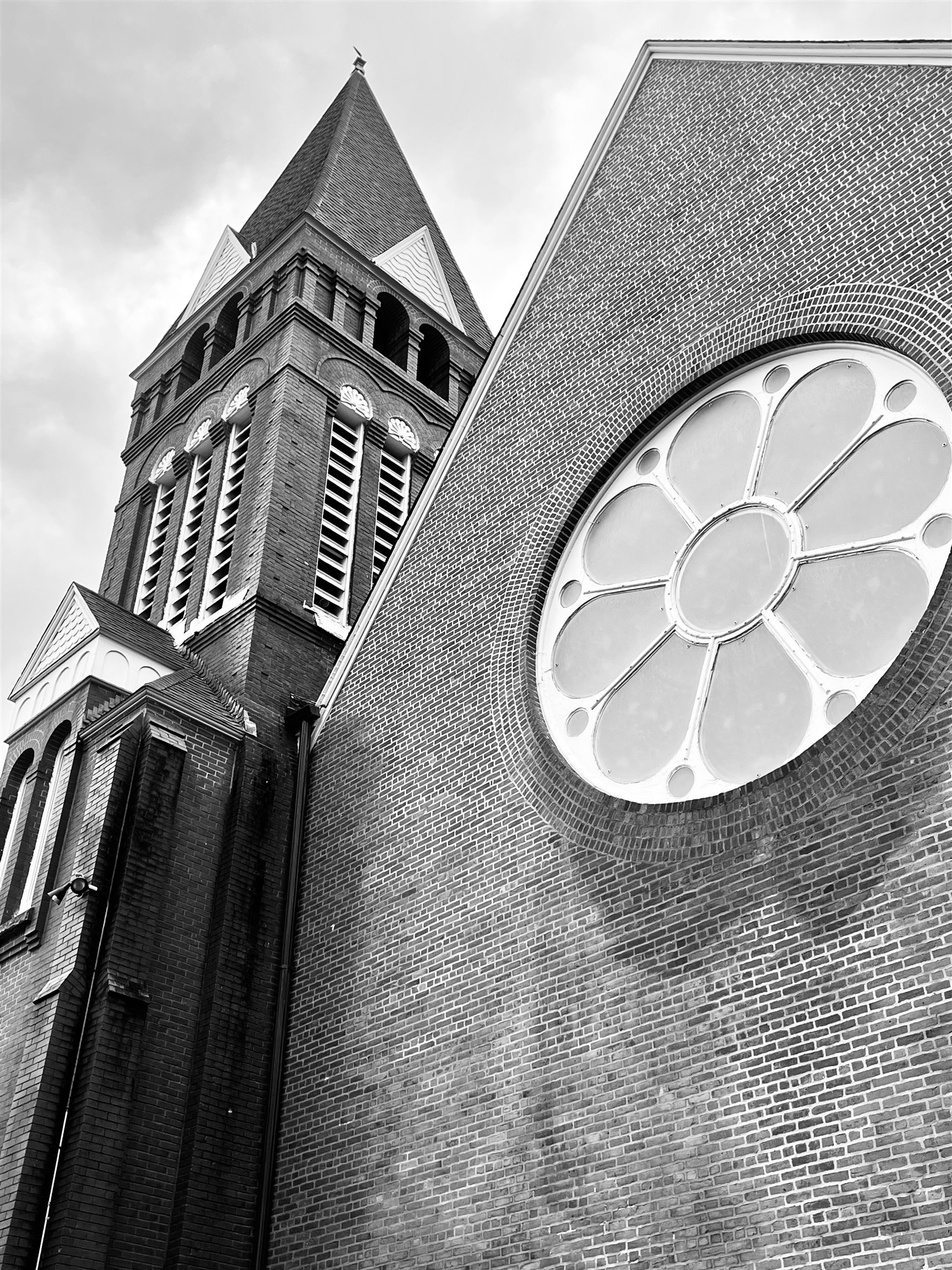 Looking up at the brick bell tower and shingled steeple of Trinity United Methodist, the great rose window set in its gable.