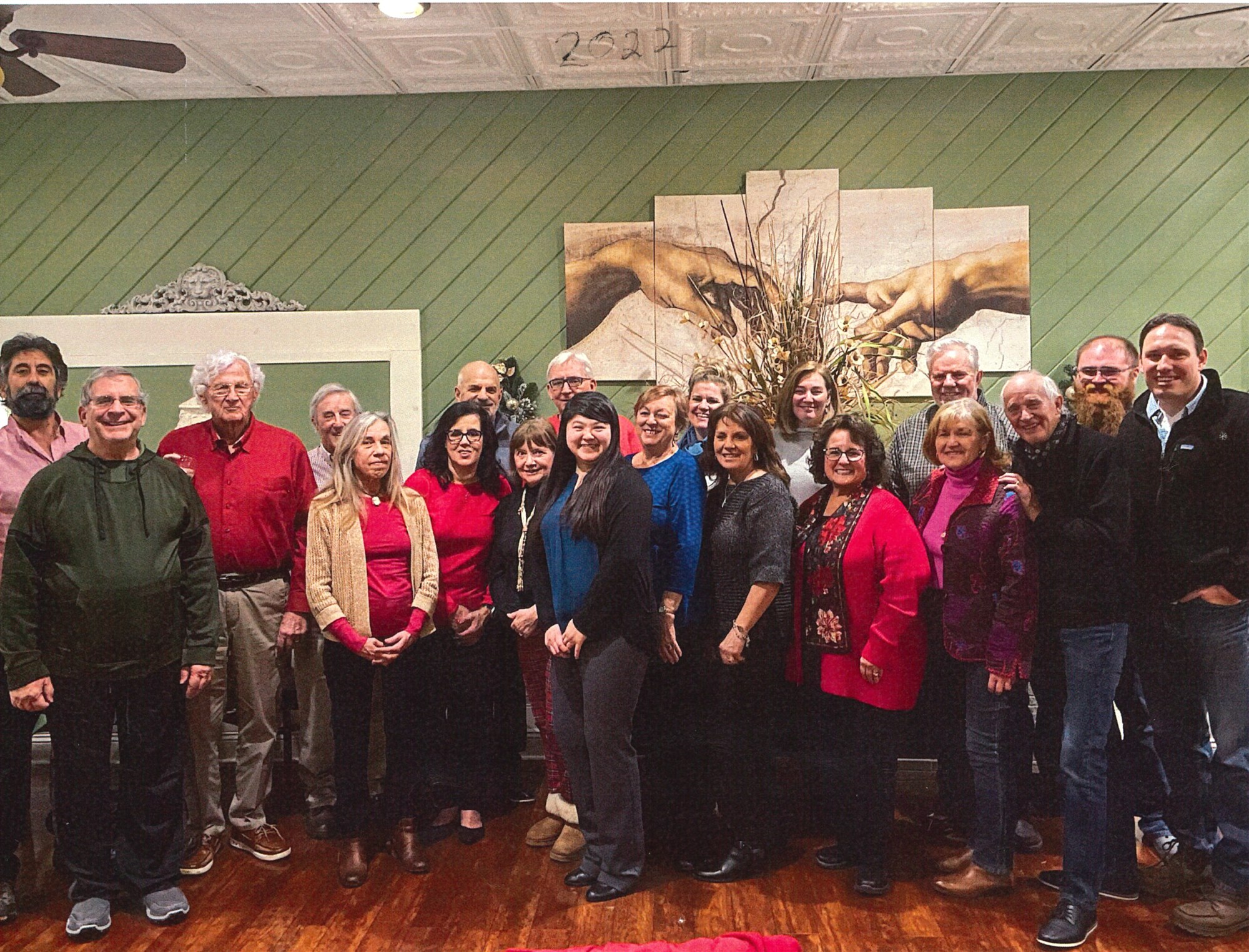 The Fiedler team in holiday reds and sweaters, gathered for a group photograph in front of a large mural on a green wall at Toscana.