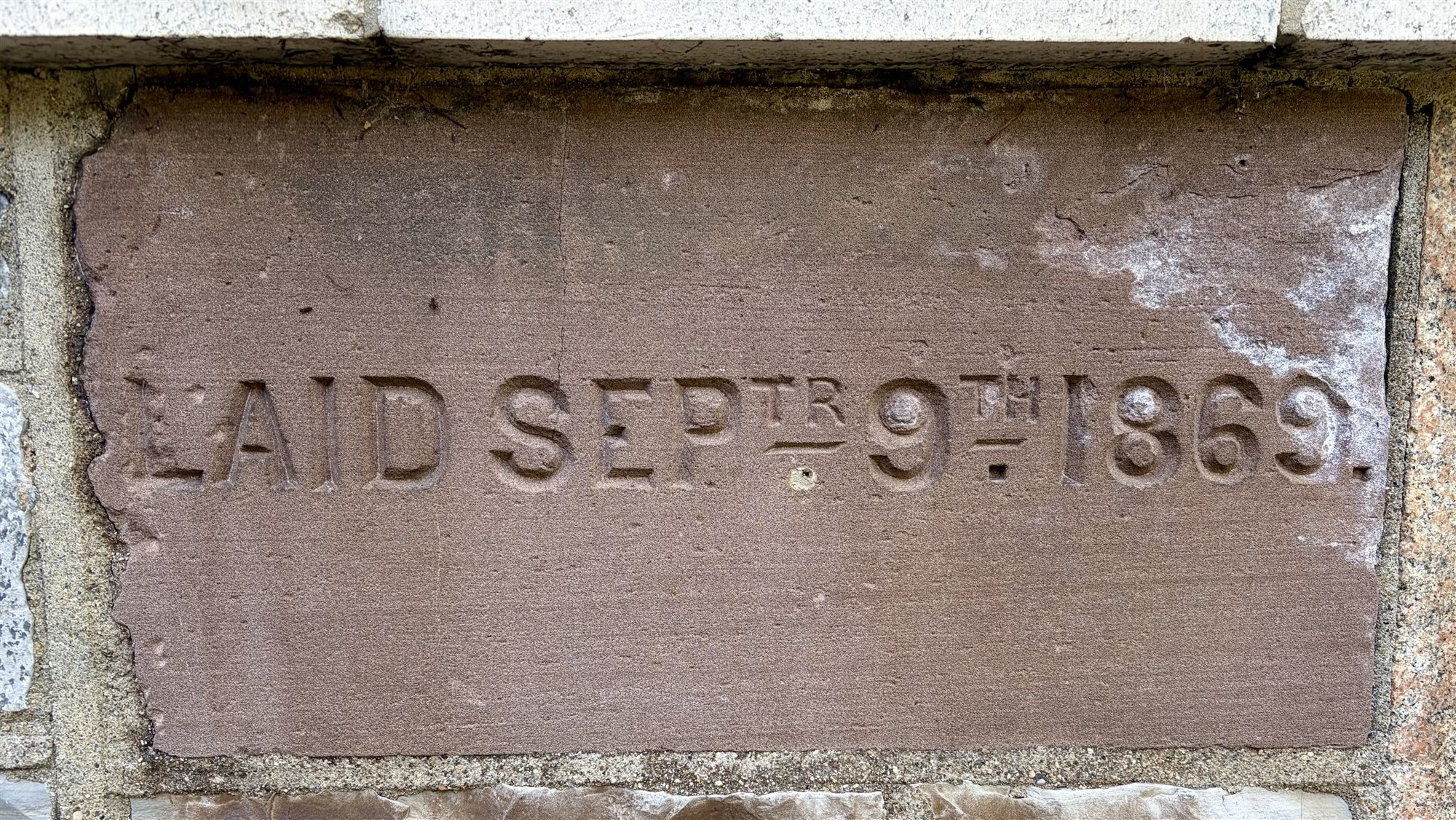 A worn brownstone cornerstone carved 'Laid Septr. 9th 1869,' set among granite blocks in a building wall.