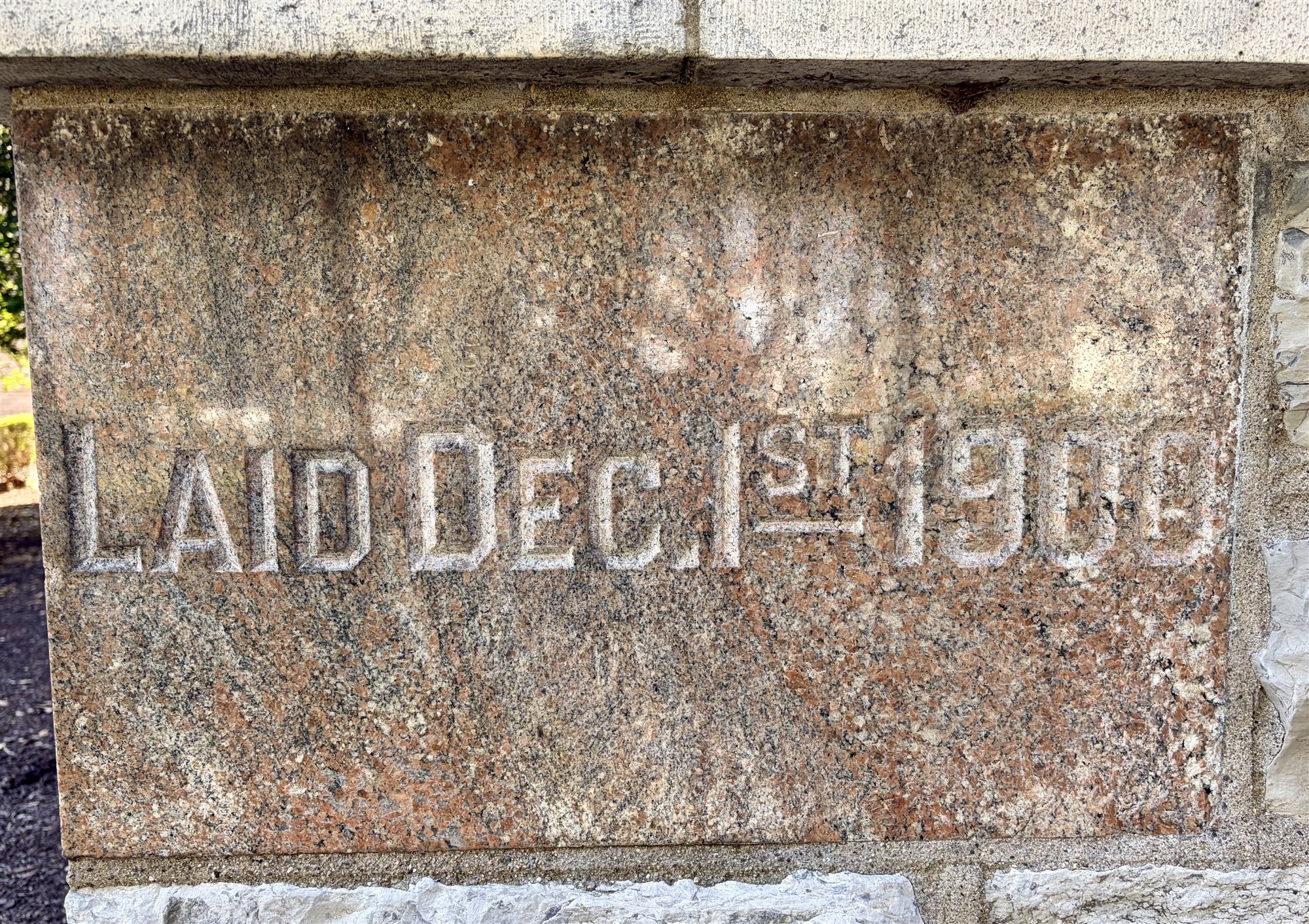 A pink granite cornerstone carved 'Laid Dec. 1st 1900,' its lettering weathered, set in the base of the rebuilt main building.