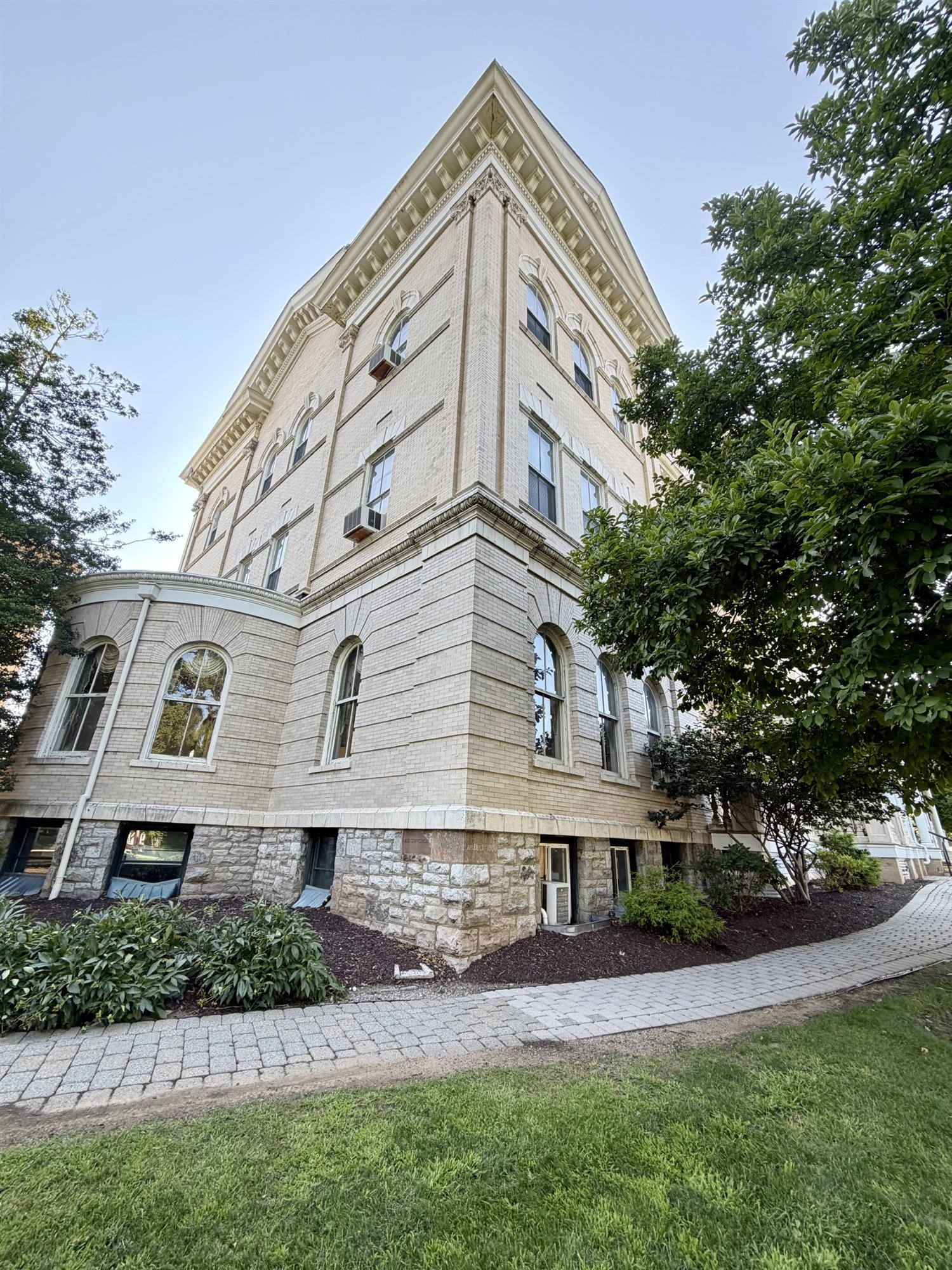 Looking up the corner of the cream-brick Seay Administration Building in evening light, rising from the rusticated stone base where the cornerstones are set.