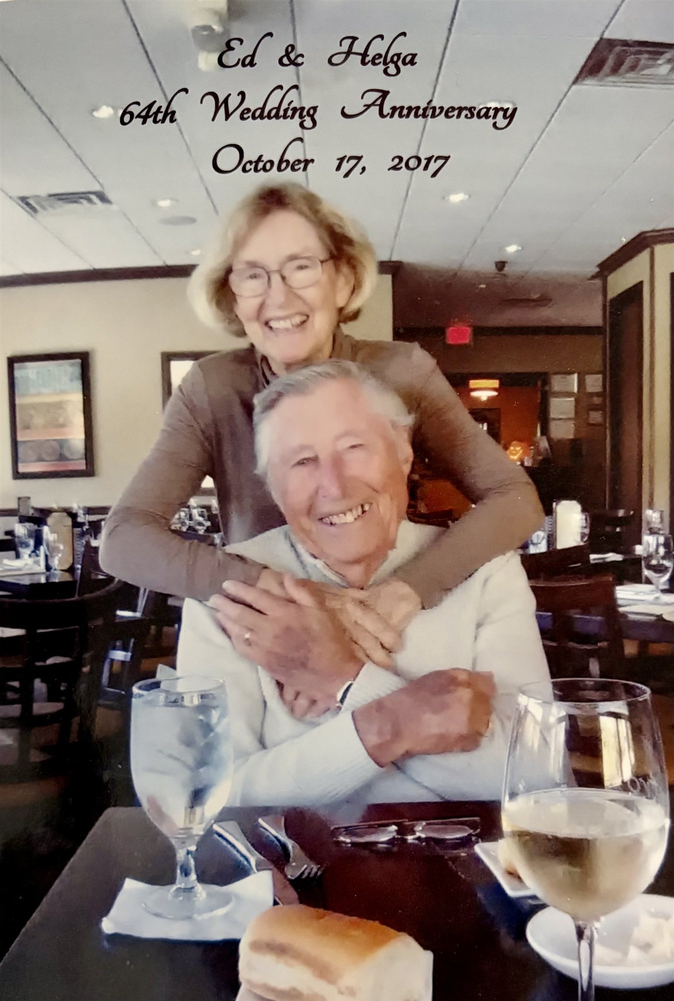 Ed and Helga Coyne embracing at a restaurant table, captioned 'Ed & Helga 64th Wedding Anniversary, October 17, 2017.'