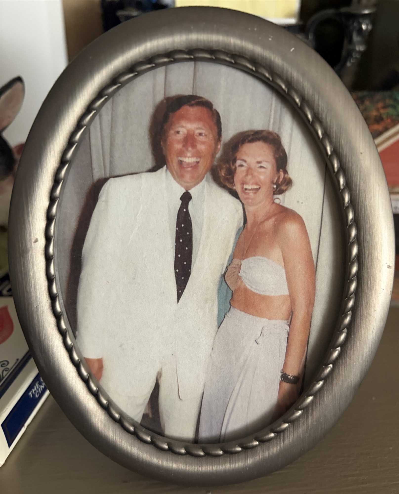 A framed oval photograph of a young Ed and Helga Coyne laughing together, he in a white suit jacket and polka-dot tie.