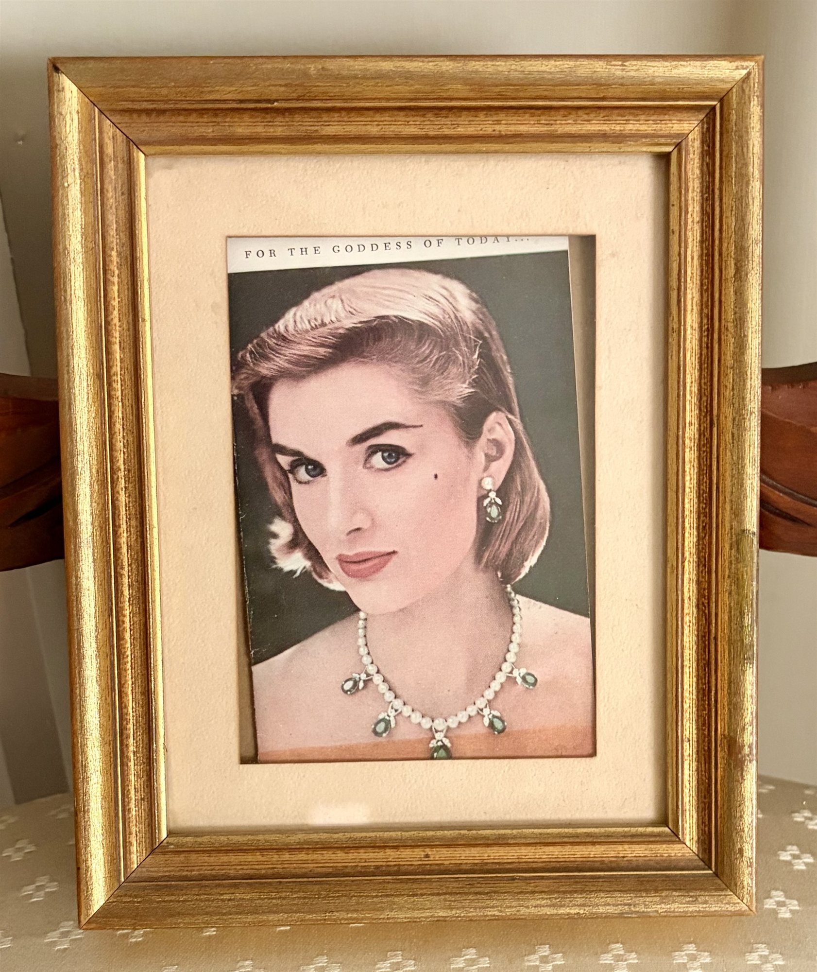 A framed vintage jewelry advertisement titled 'For the Goddess of Today,' with Helga Coyne modeling an emerald and pearl necklace.