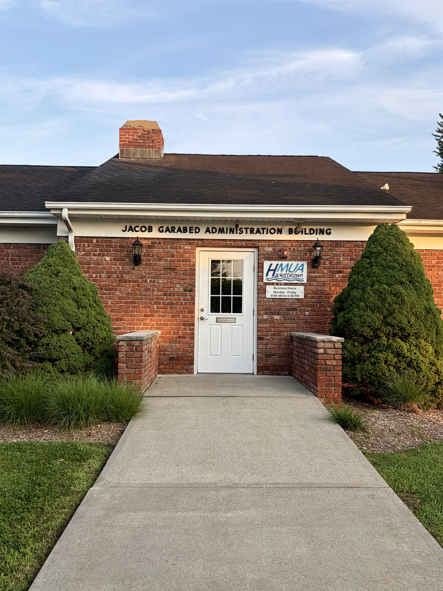 The brick entrance of the HMUA building in early-morning light, a white door beneath black metal letters reading 'Jacob Garabed Administration Building.'