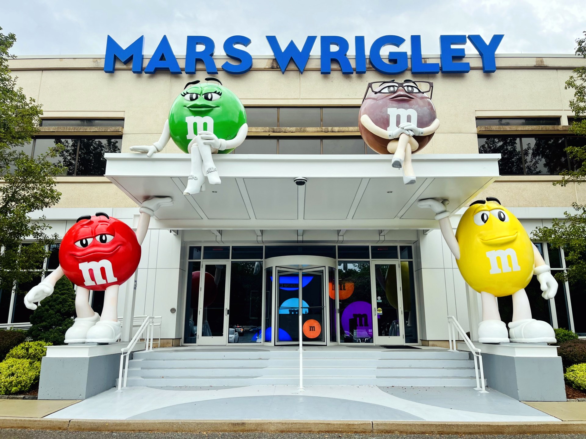 The Mars Wrigley building entrance in Hackettstown, with giant red, yellow, green, and brown M&M character statues set around the doorway beneath the company sign.